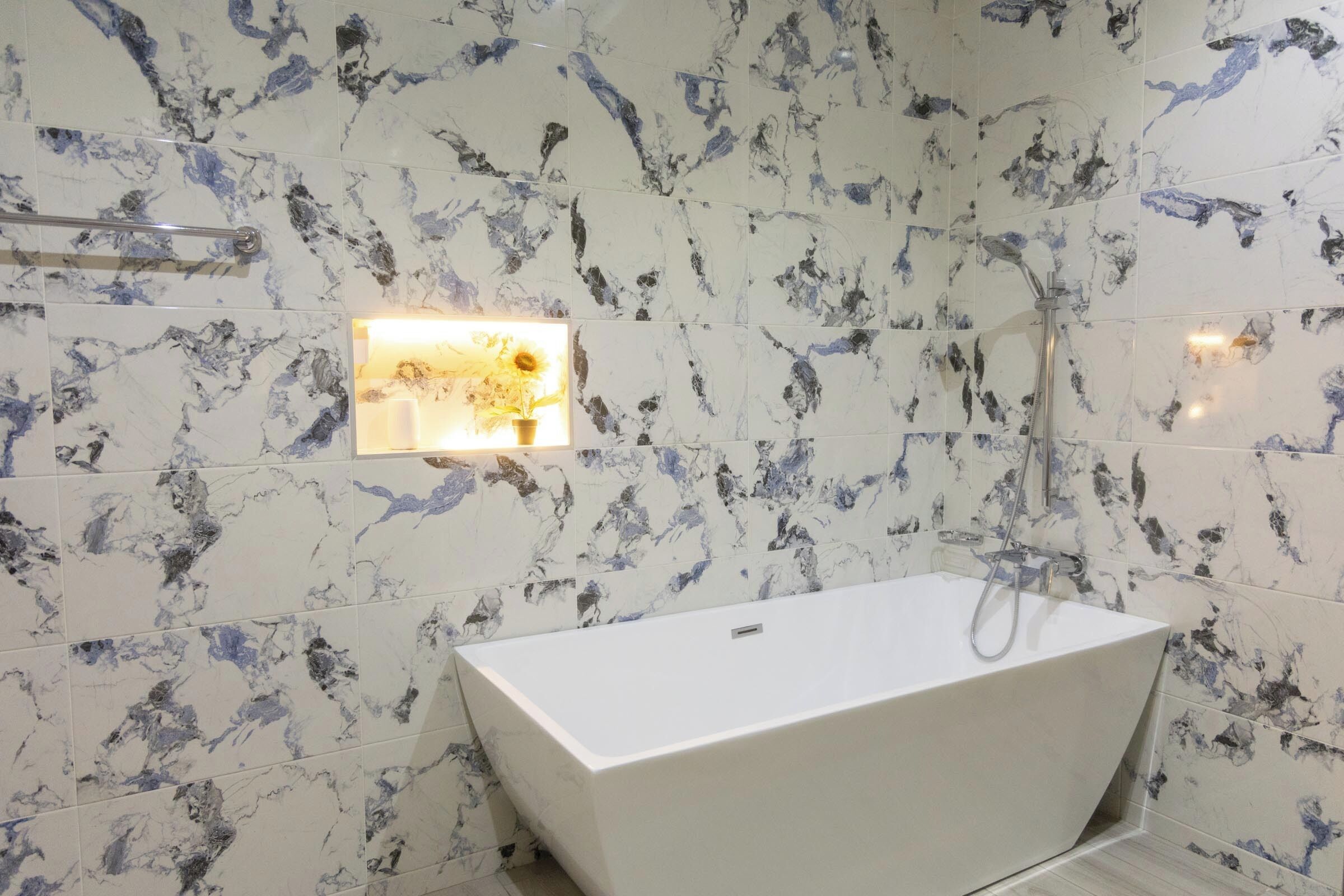 A modern bathroom with a freestanding bathtub, marble-patterned walls, and a wall-mounted light fixture.