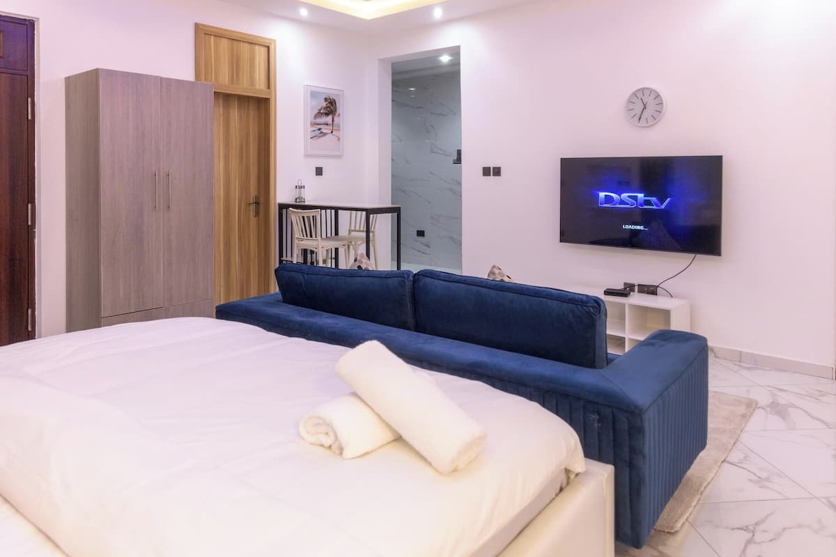 Une chambre moderne avec un grand lit, un canapé bleu, une télévision et une armoire.