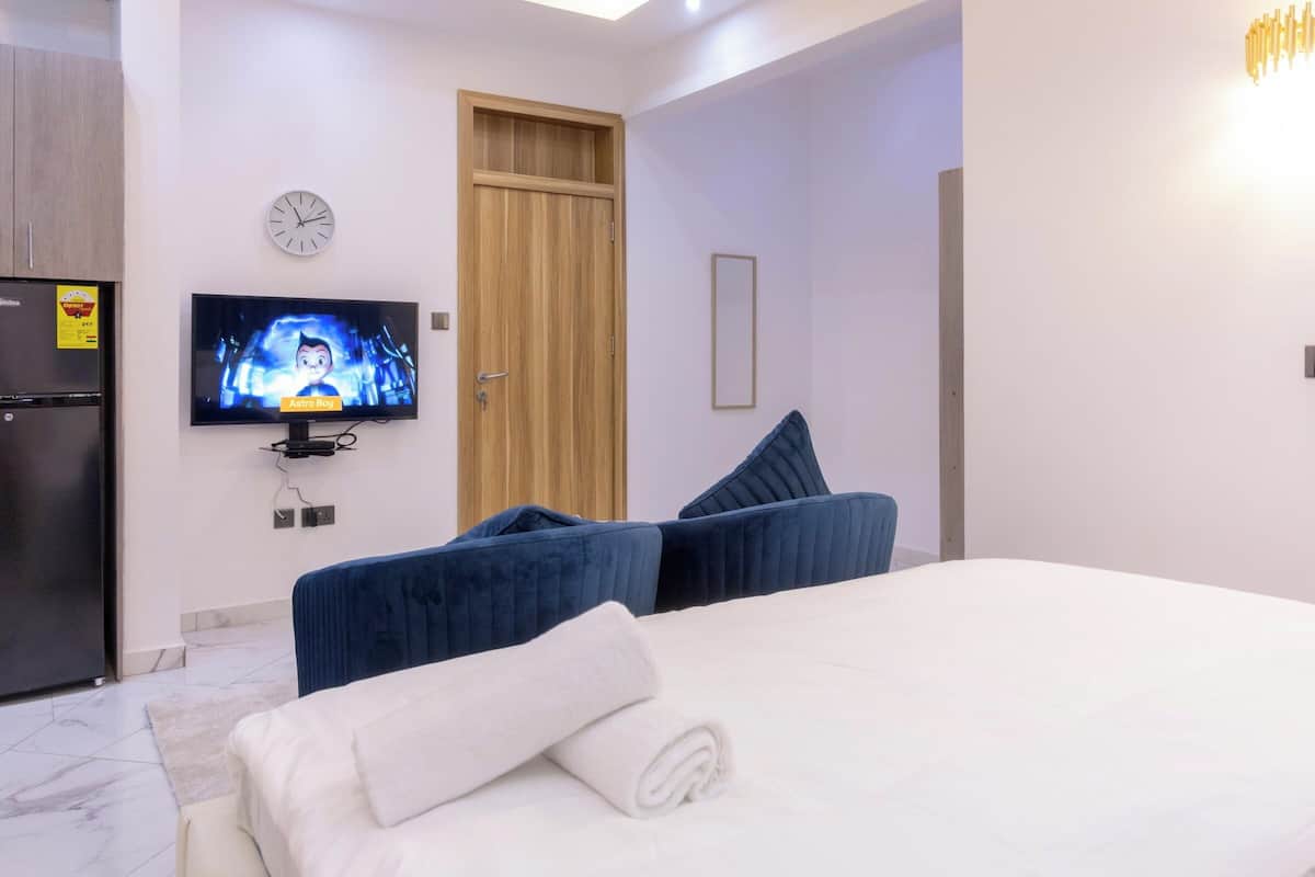 Une chambre d’hôtel avec un lit, une télévision, une porte en bois et une horloge au mur.