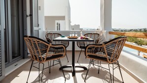 Ein Balkon mit Tisch und vier Korbstühlen, mit Blick auf die Küste.