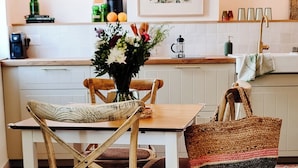 Un comedor con una mesa y sillas de madera, un florero y una cocina al fondo.