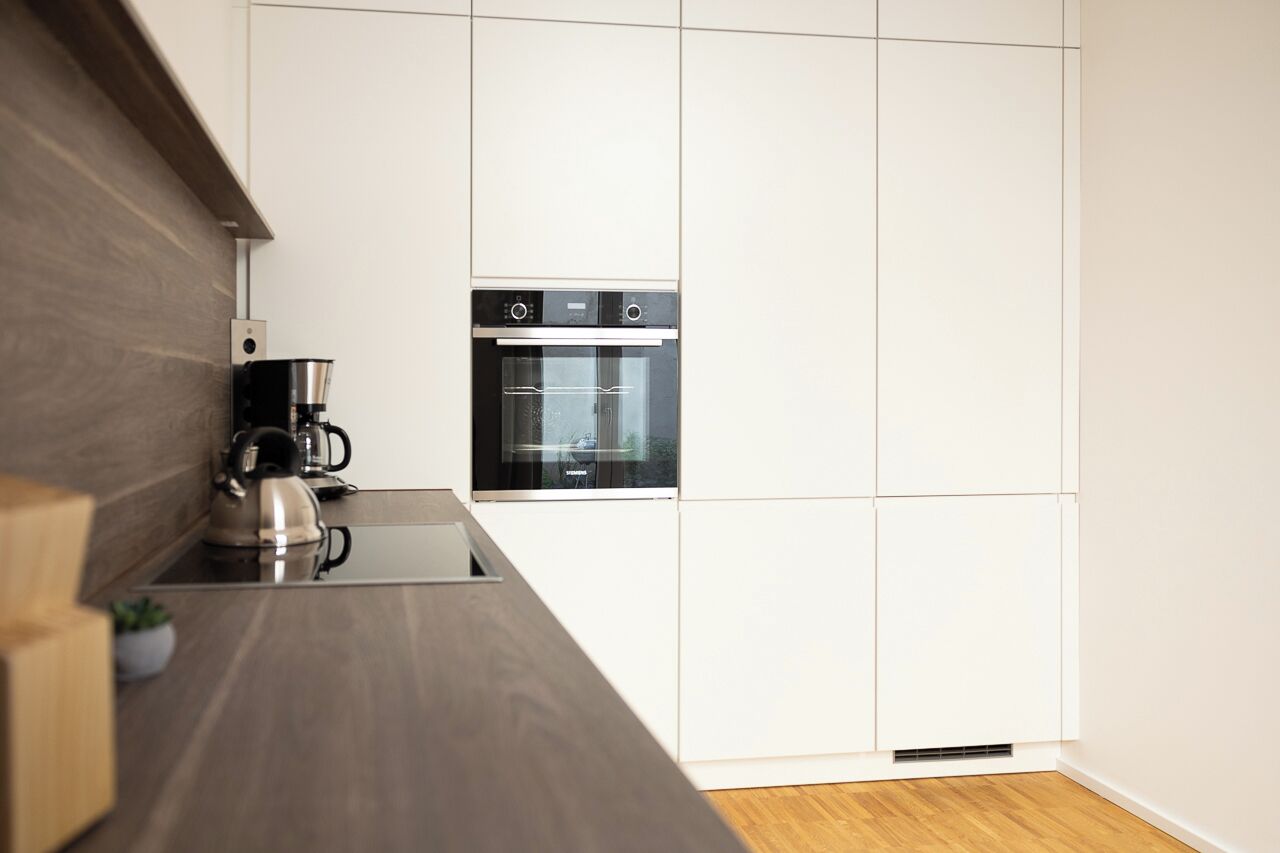 A modern kitchen with a built-in oven and coffee maker, wooden countertop, and white cabinetry.