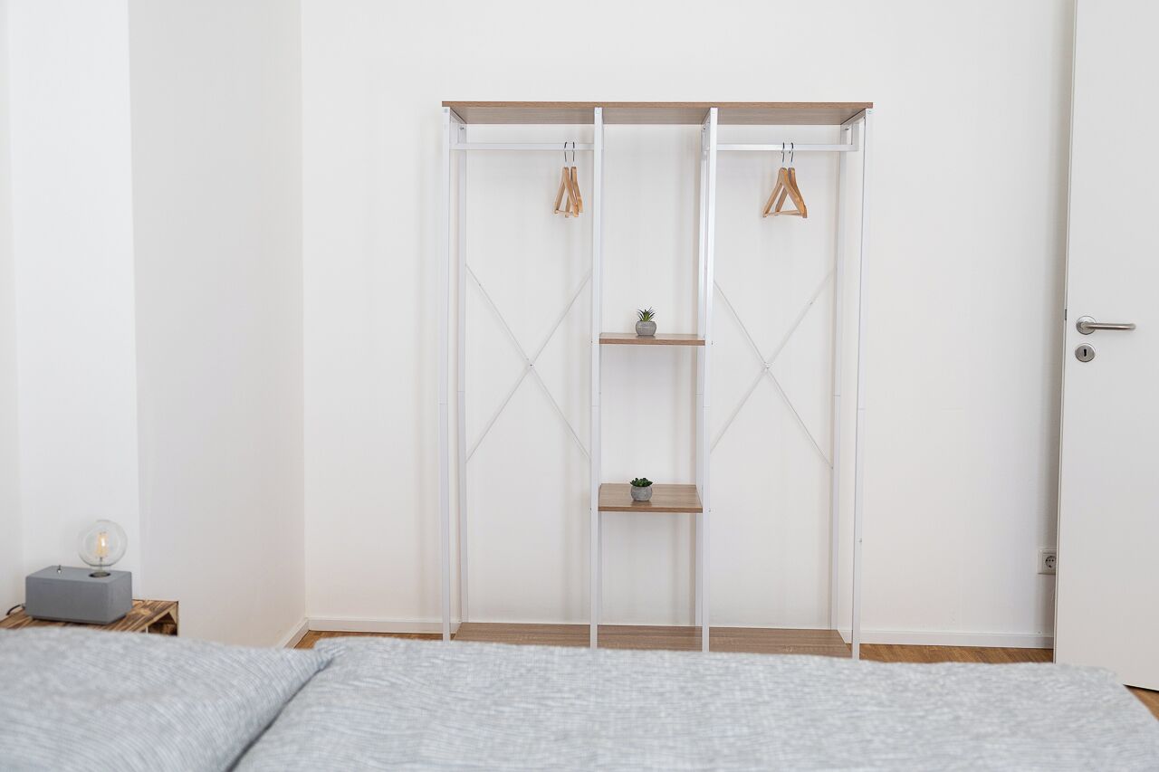 A bedroom with a bed, a wardrobe with shelves, and a bedside table with a lamp.