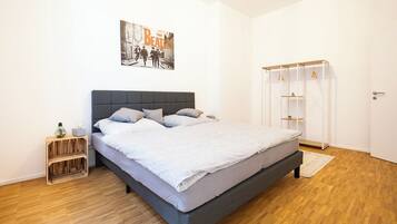 Ein modernes Schlafzimmer mit grauem Bett, einem Holznachttisch, einem an der Wand befestigten Kleiderschrank und einem Beatles-Poster.