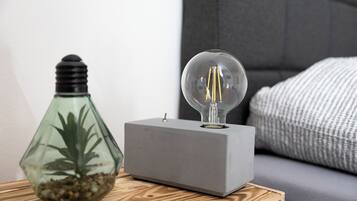 Una camera moderna con una radio grigia squadrata su un tavolino in legno, una lampada in vetro trasparente con una lampadina e una bottiglia di vetro con una pianta.