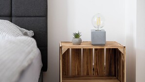 A neatly made wooden nightstand with a potted plant and a modern light fixture.