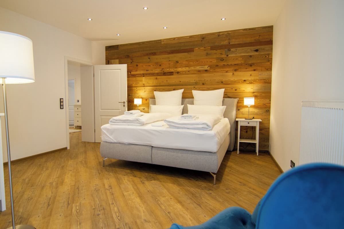 Een moderne slaapkamer met een houten paneelwand, een bed met witte lakens, een nachtkastje met een lamp en een radiator.