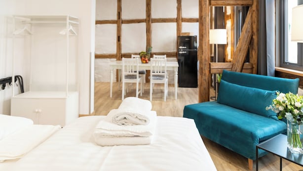 A hotel room with a bed, a teal sofa, a dining table with chairs, and a kitchen area. - Schiefer Suite Hotel & Apartment (Goslar)