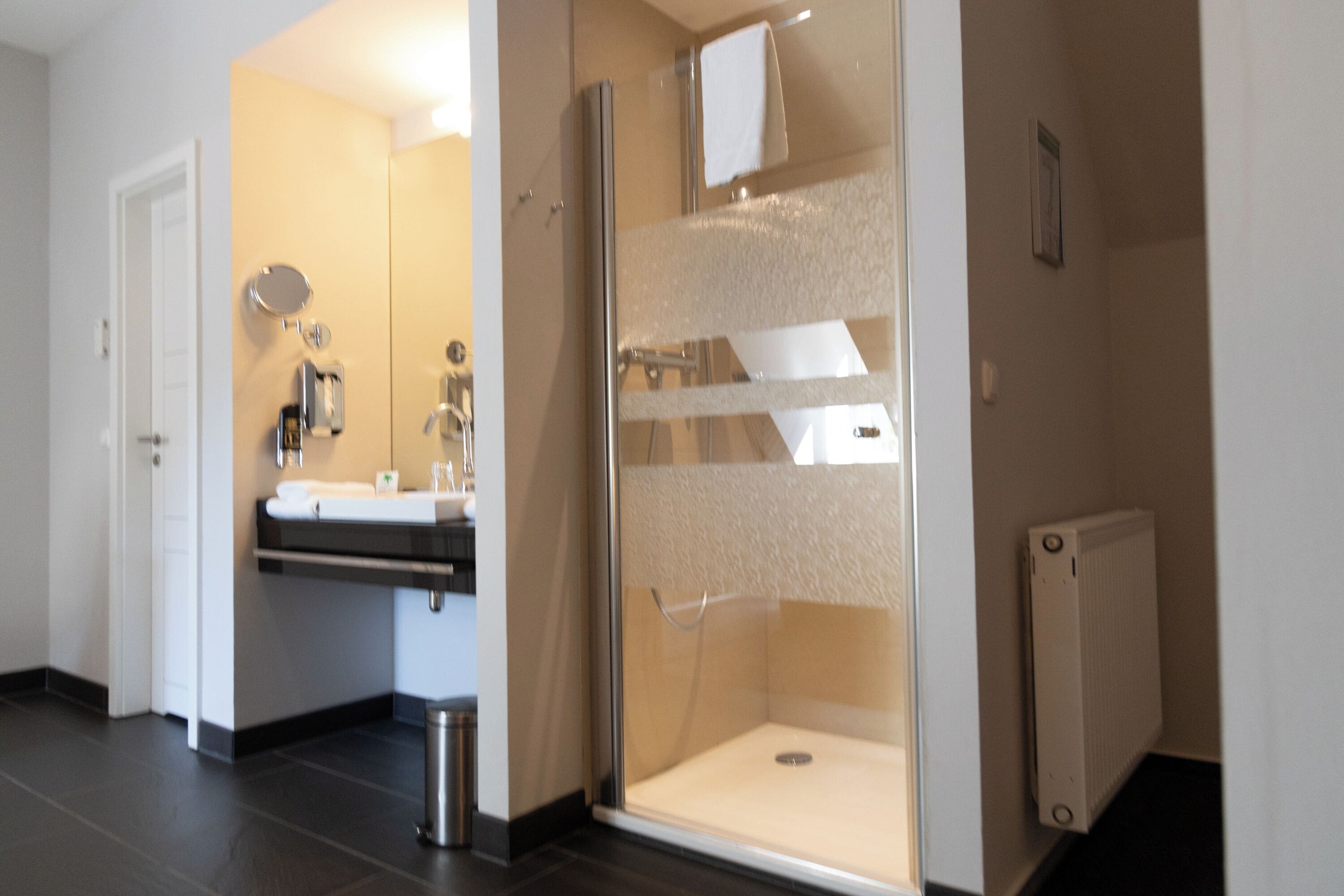A modern bathroom with a glass-enclosed shower, a sink with a mirror, and a towel hanging on the wall.
