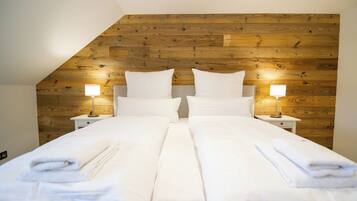A double bed with white linens and towels, two bedside tables with lamps, and a wooden sloped ceiling.