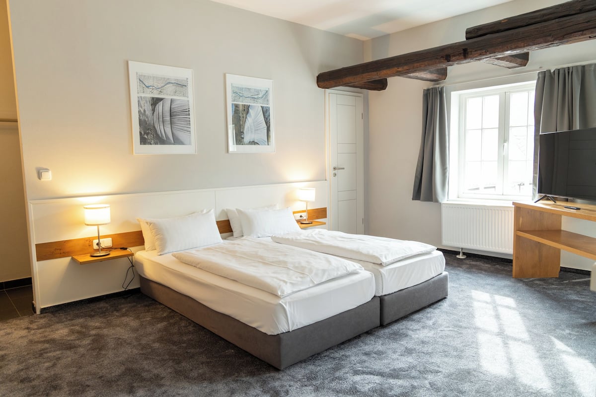 Een hotelkamer met een tweepersoonsbed, nachtkastjes, een bureau, een televisie en kunstwerken aan de muur.