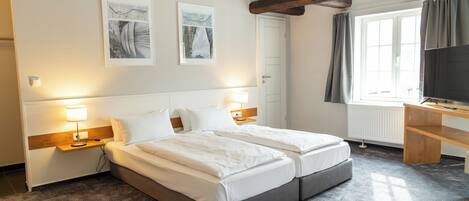 Habitación de hotel con cama doble, mesitas de noche, escritorio, televisor y obras de arte en las paredes.