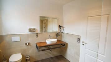 Et moderne badeværelse med toilet i hvid, vaskebord i træ med vask i hvid, og et spejl over vasken.