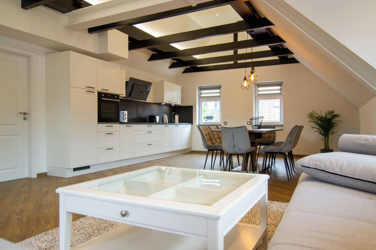 Een moderne keuken met witte kasten, een eethoek met een tafel en stoelen, en een salontafel met glazen blad.