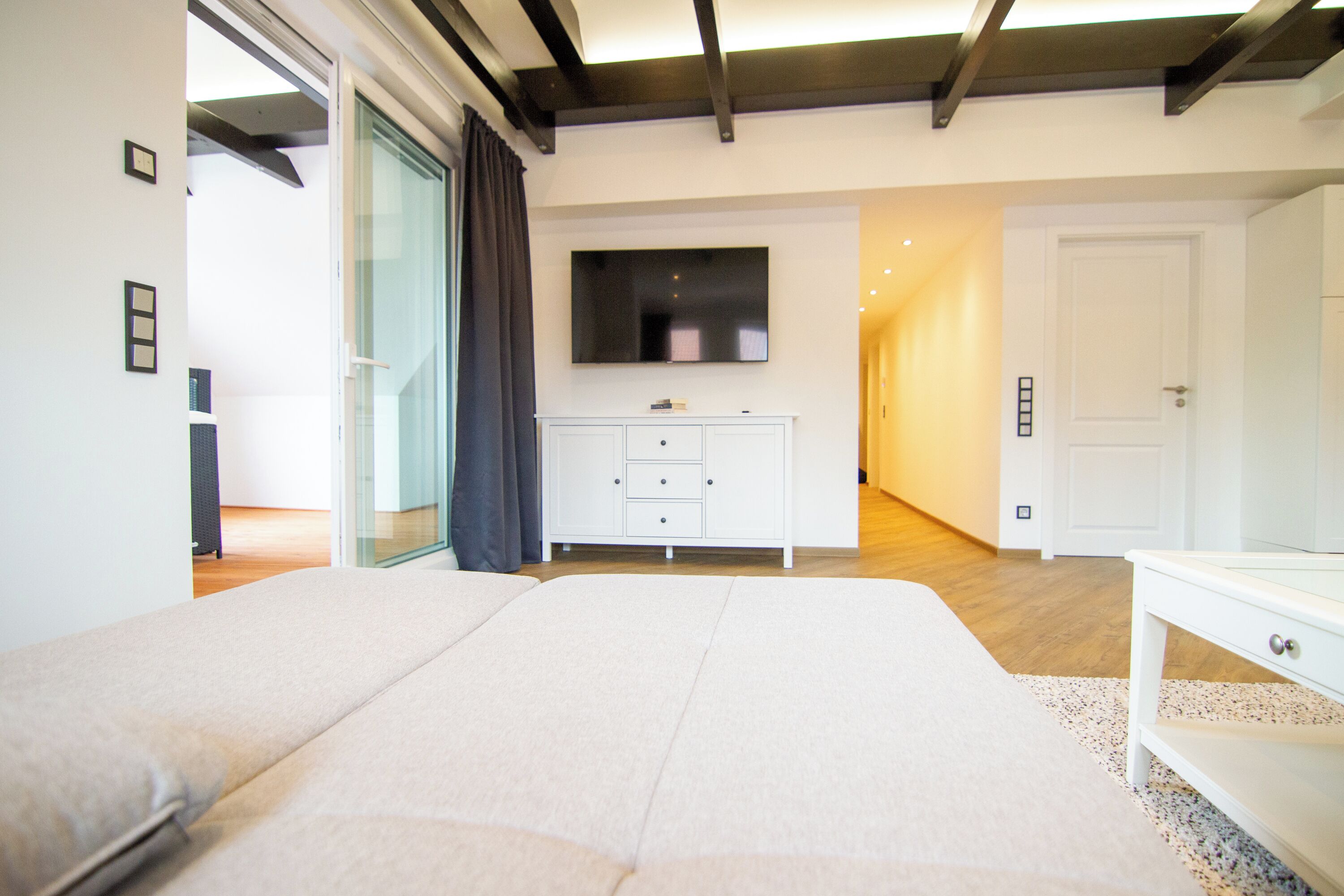 A modern bedroom with a large bed, a TV mounted on the wall, and a white dresser.