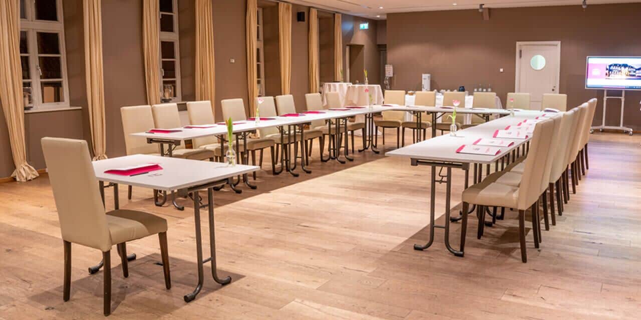 Een vergaderzaal met lange tafels en stoelen, een projectiescherm en een whiteboard.