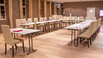 Een vergaderzaal met lange tafels en stoelen, een projectiescherm en een whiteboard.