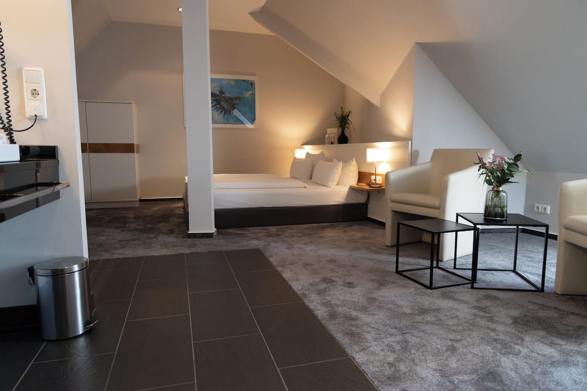 Een moderne, goed verlichte kamer met een bed, een slaapbank, een klein tafeltje en een prullenbak.