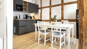 A modern kitchen with dark cabinets, a white dining table, and chairs. - Schiefer Suite Hotel & Apartment (Goslar)