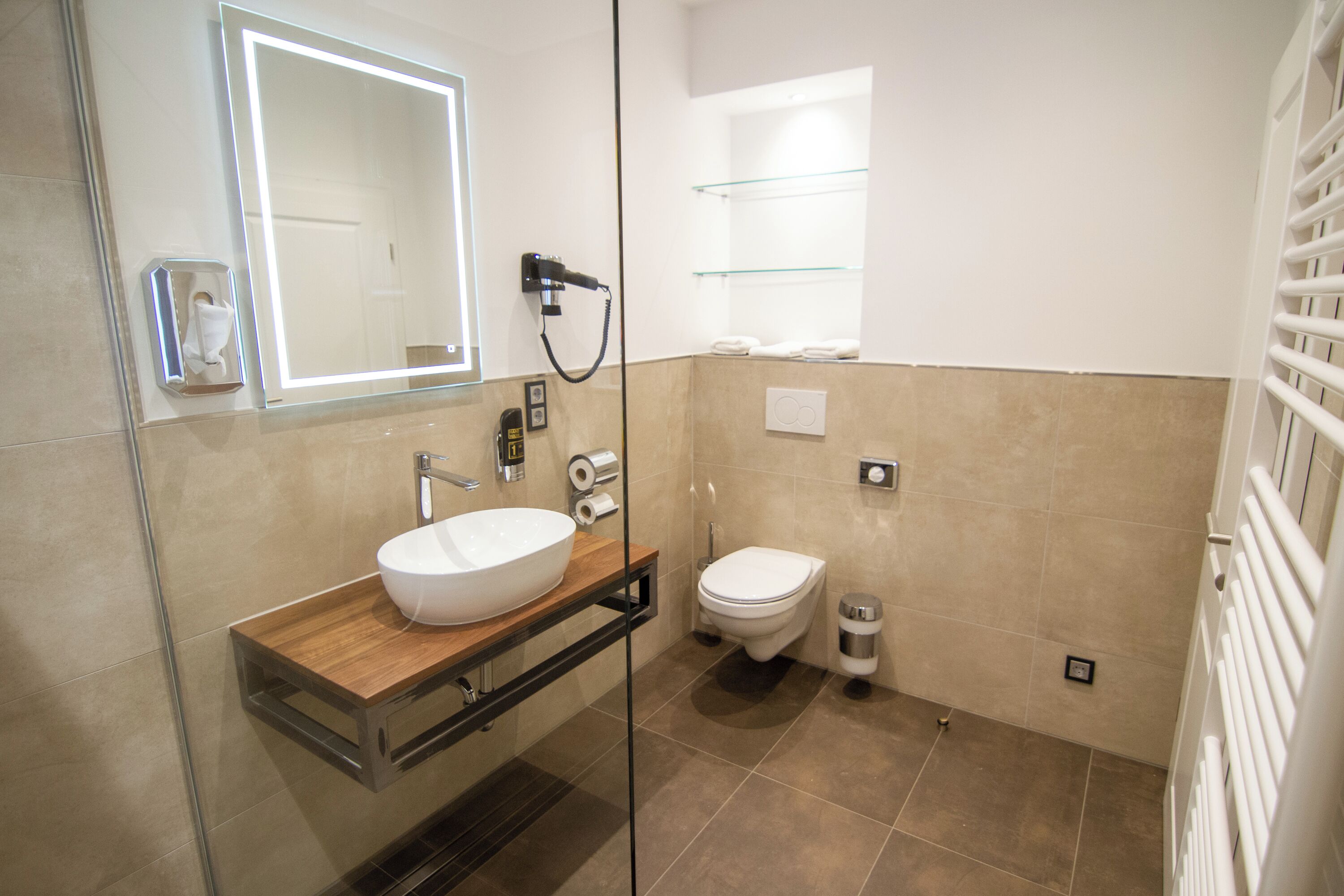 A modern bathroom with a glass-enclosed sink, a toilet, and a mirror with built-in lighting.