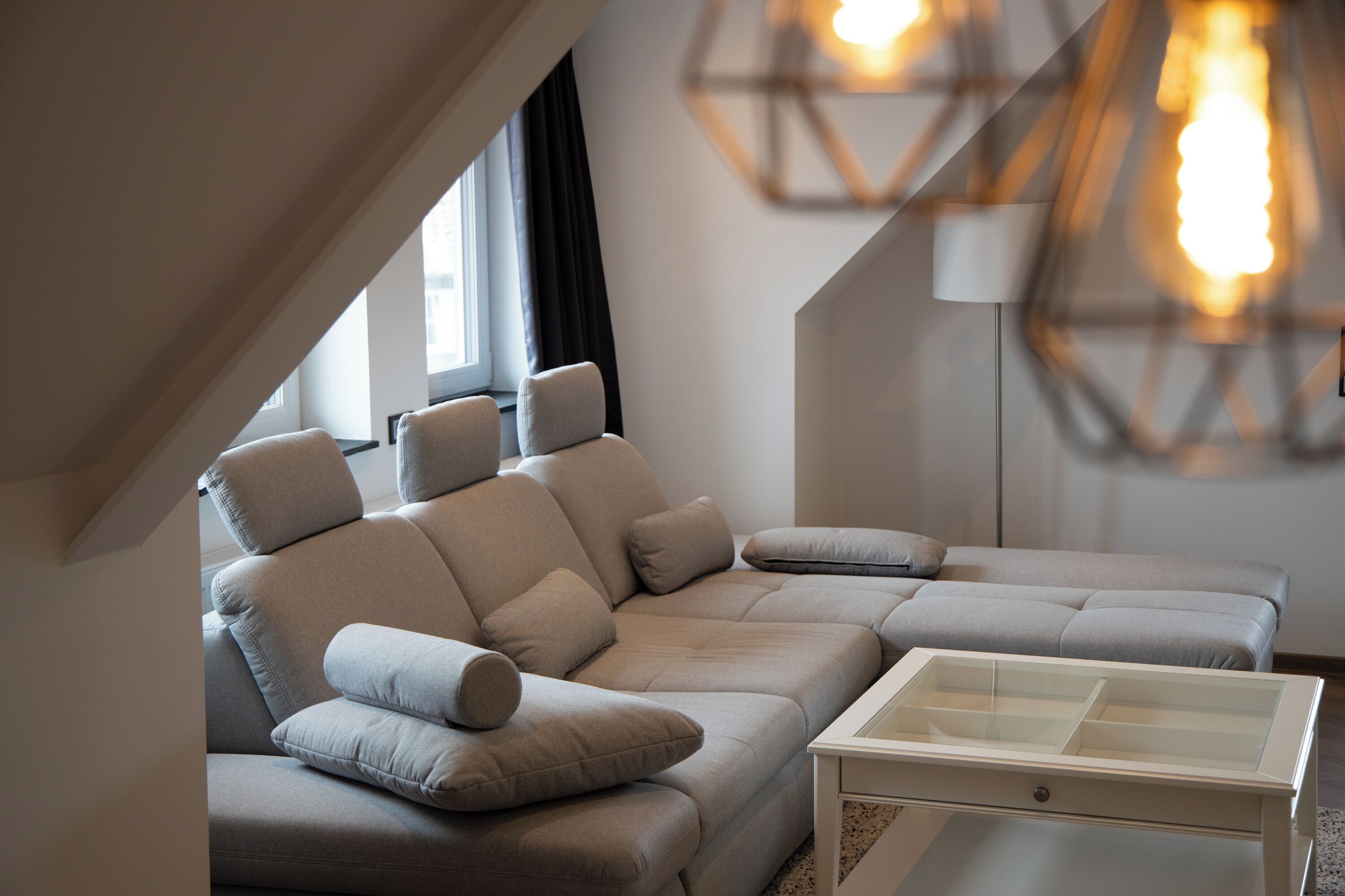 A modern living room with a sectional sofa, a glass coffee table, and pendant lighting.