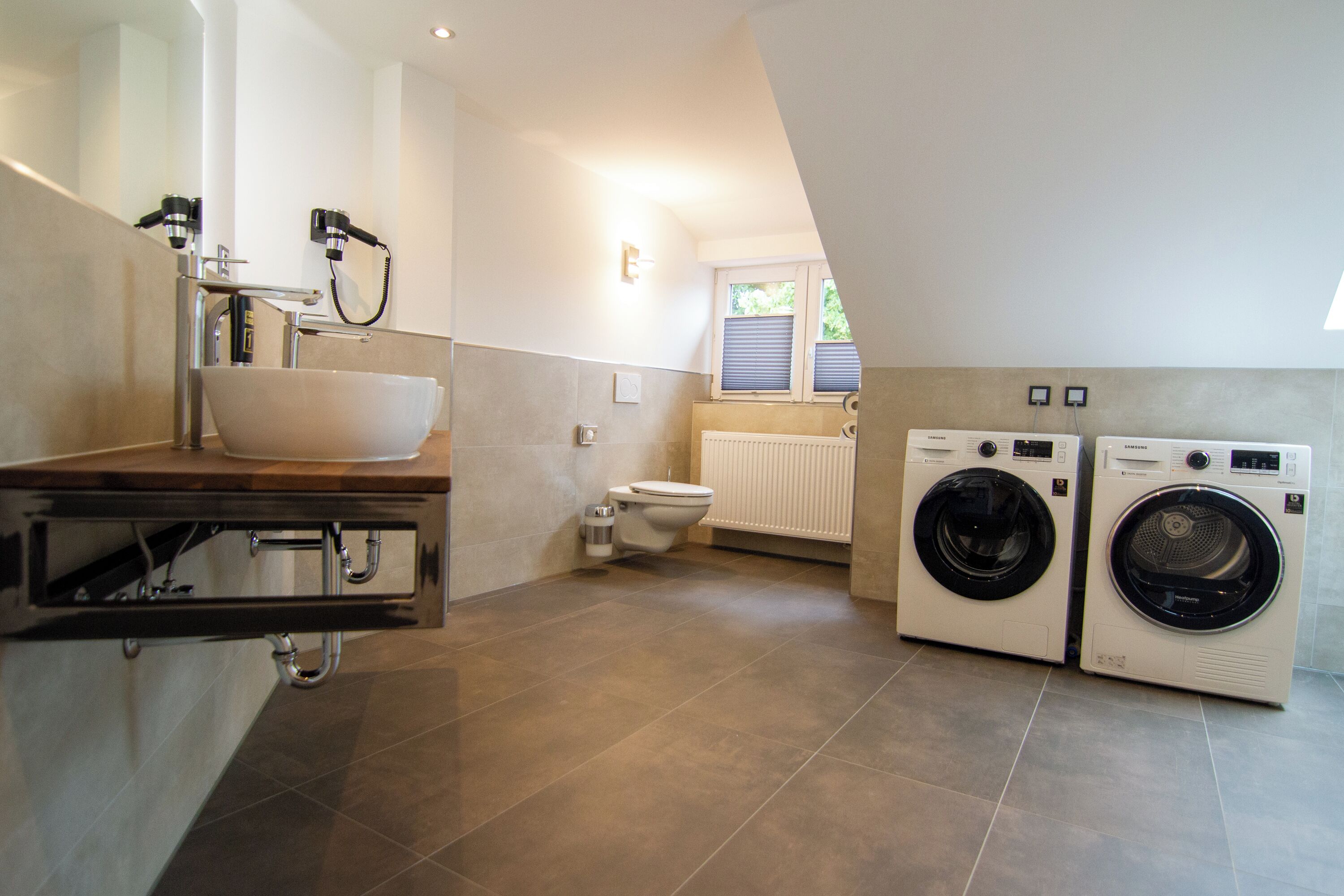 A compact bathroom with a sink, toilet, and two wall-mounted washing machines.