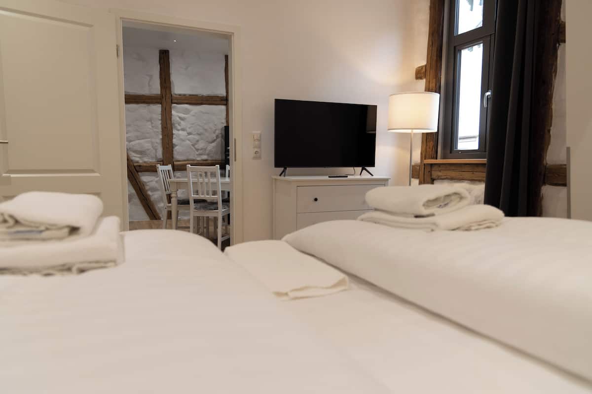 Een hotelkamer met twee bedden, een tv op een standaard, een bureau met een stoel, en een raam met gordijnen.