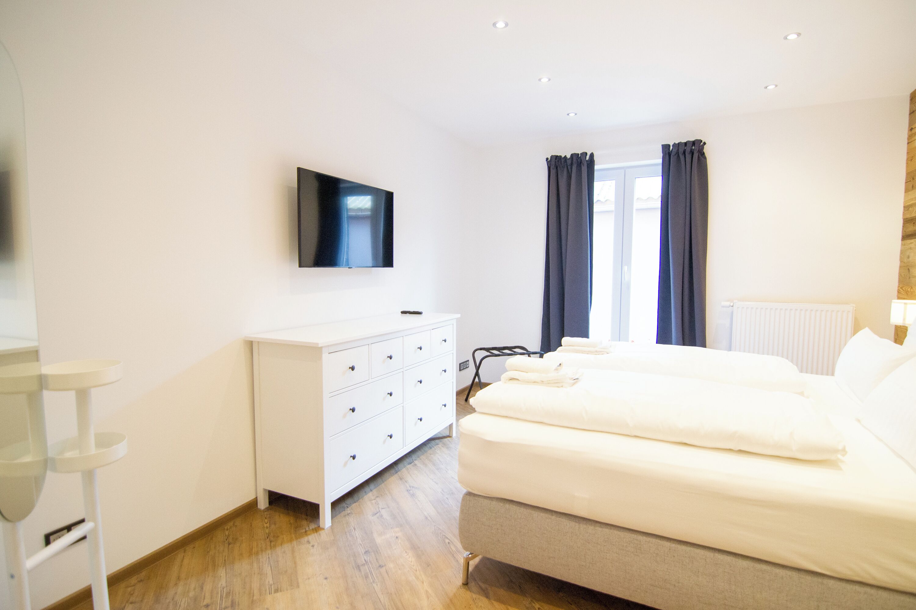 A modern bedroom with a bed, a dresser, a flat-screen TV, and a window with curtains.