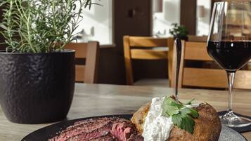 A plate with steak and a baked potato topped with sour cream and garnish, a glass of red wine, and a potted plant on a table.