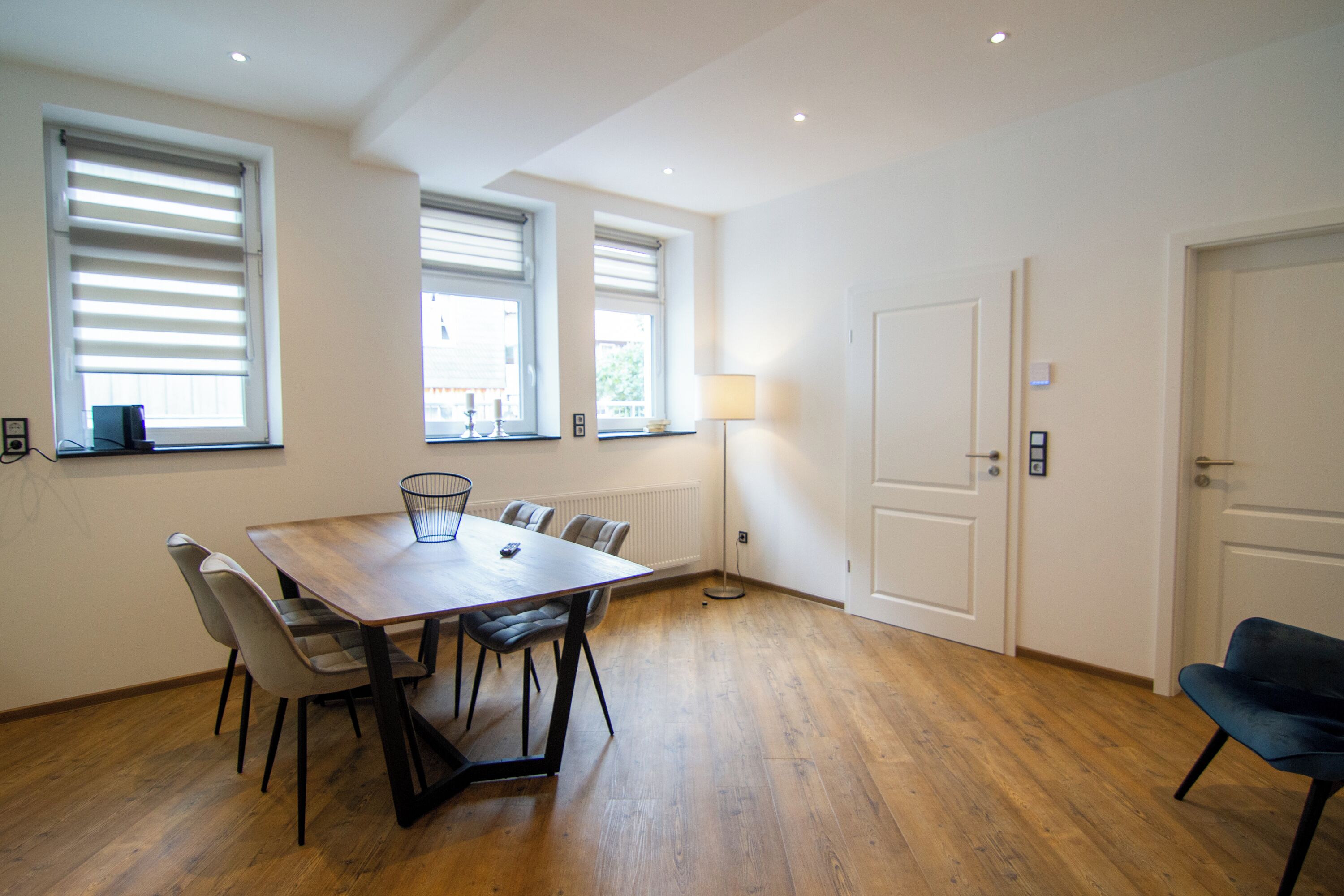 A room with a wooden dining table, chairs, a lamp, and two doors.
