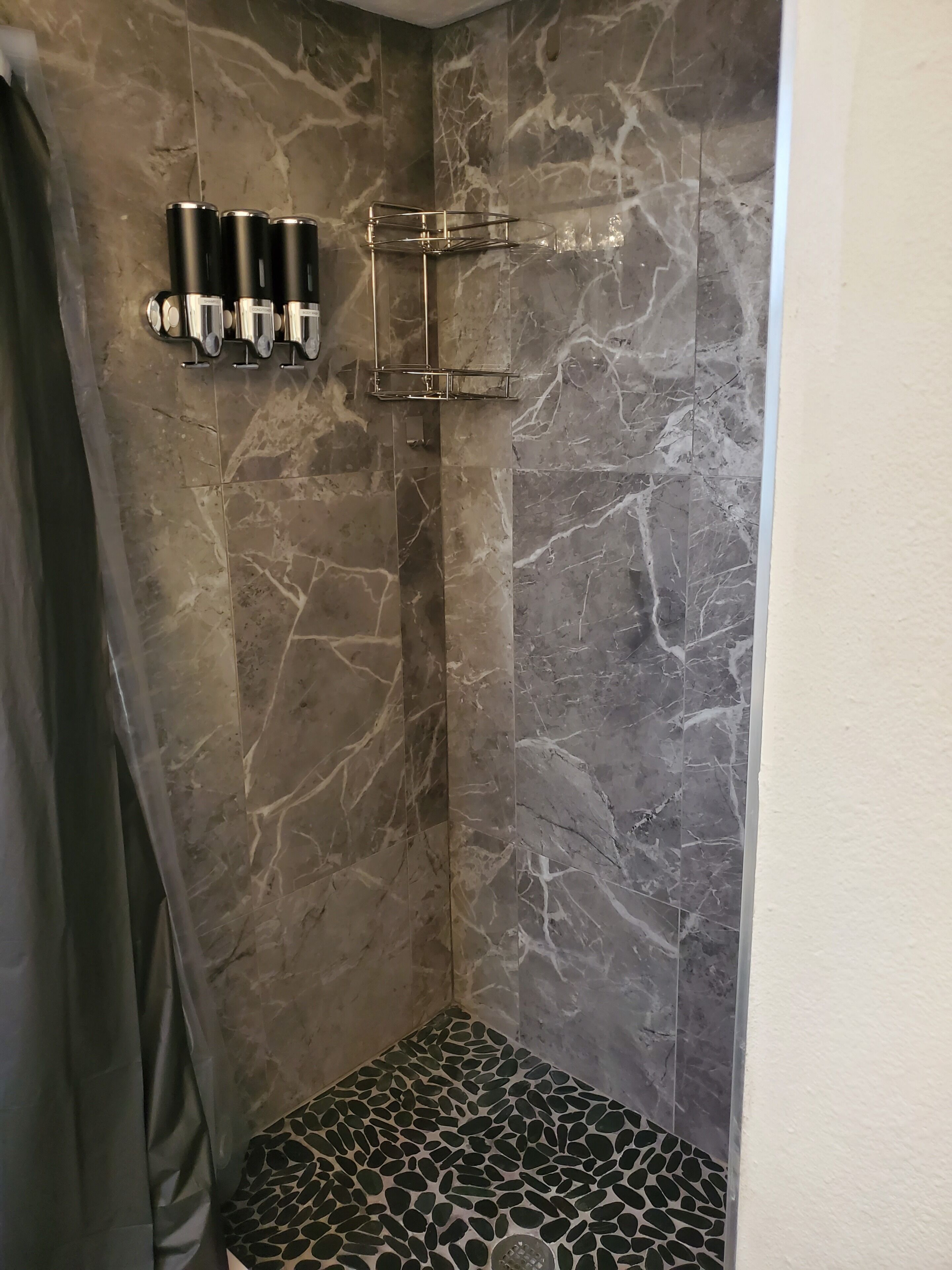 Area doccia con parete in marmo, soffione metallico e portasapone.