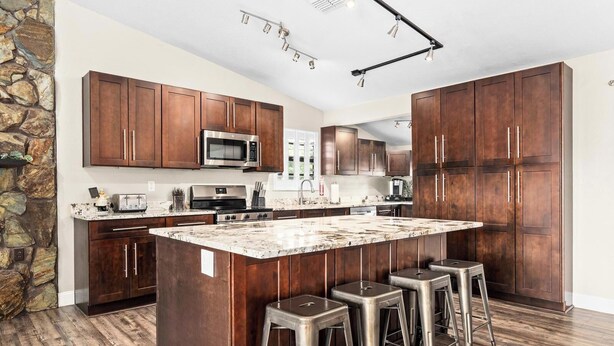 A modern kitchen with dark wood cabinets, a large island with bar stools, stainless steel appliances, and a stone accent wall. - Florida Life on the water with game room, heated pool, kayaks +
Pet friendly!! (Palm Harbor)