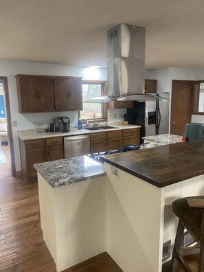 A kitchen with wooden cabinets, granite countertops, a stainless steel range hood, and a built-in dishwasher.