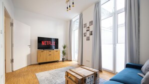 A modern living room with a wooden coffee table, a blue sofa, and a flat-screen TV on a wooden cabinet.