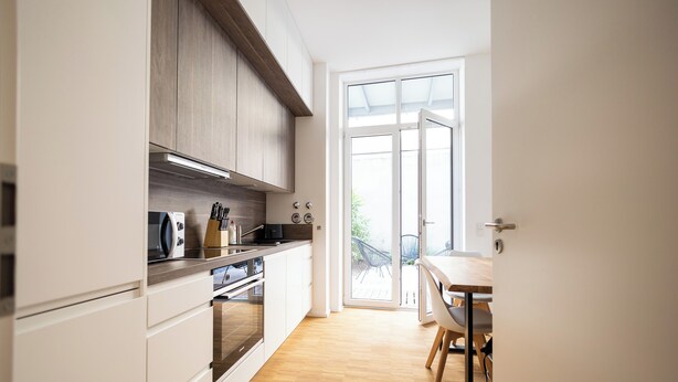 A modern kitchen with white cabinets, a wooden countertop, and a dining area with a table and chairs.