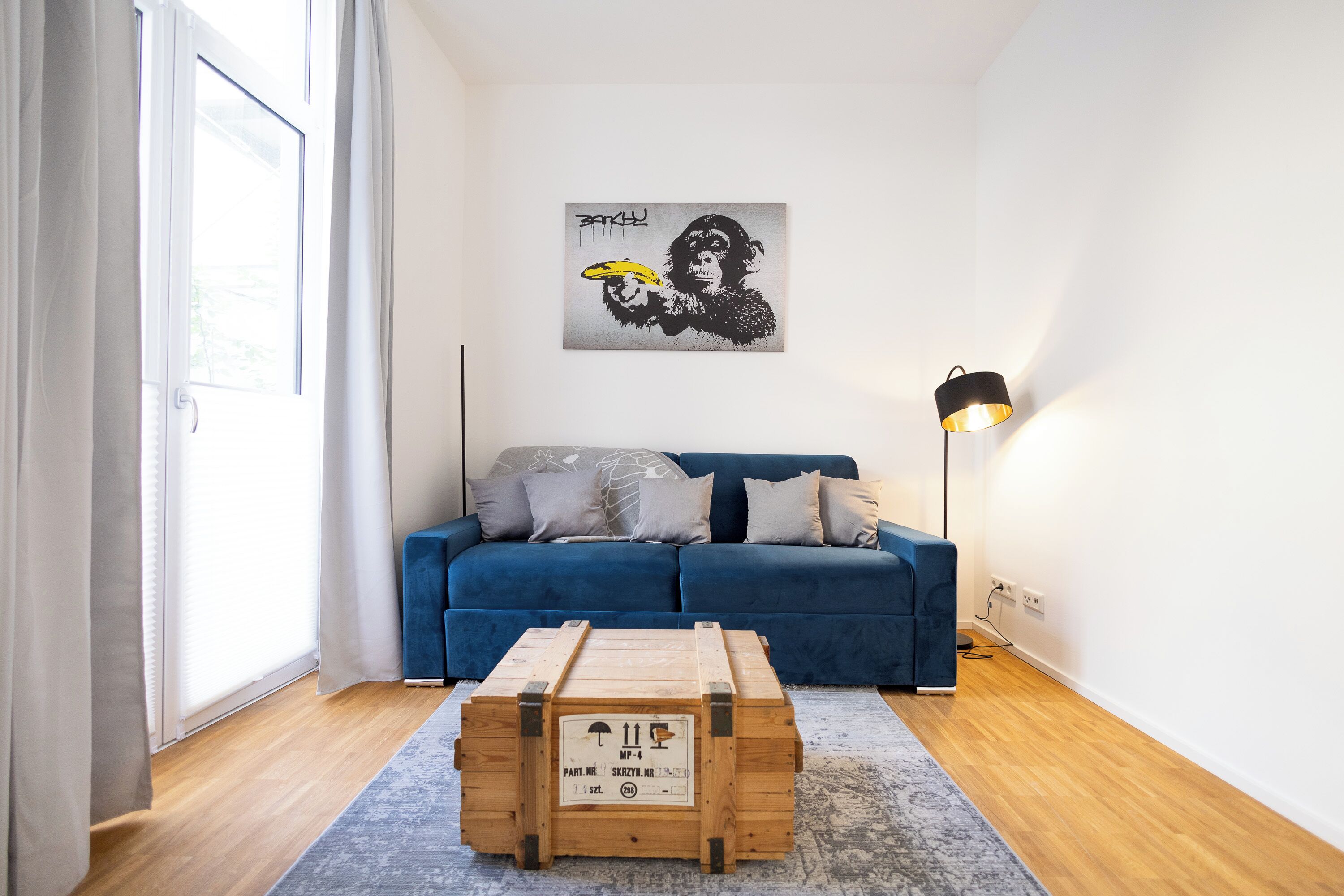 A modern living room with a blue sofa, a wooden crate, and a wall art of a gorilla holding a banana.