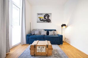Ein modernes Wohnzimmer mit einem blauen Sofa, einer Holzkiste und einem Wandbild einer Gorilla, die eine Banane hält.