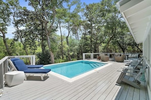 A poolside area with a rectangular pool, lounge chairs, and a deck.