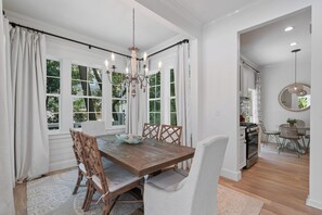 A dining room with a wooden table, white chairs, and a chandelier.