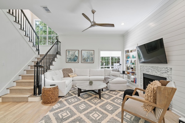 A spacious living room with a staircase, a fireplace, and a television mounted on the wall.