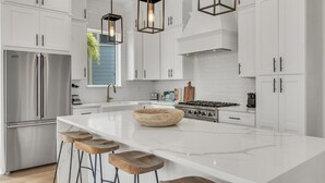 Une cuisine moderne avec des meubles blancs, un grand îlot central, des tabourets de bar et des luminaires suspendus.