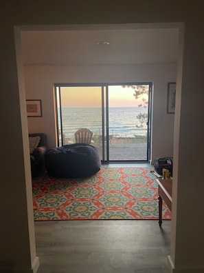 A room with a large sliding glass door leading to a balcony with a view of the sea. There is a bean bag chair and a small table with a chair on the balcony. - MidCentury Beach House (Spring Lake)