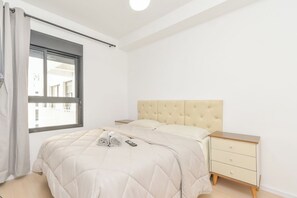 Een minimalistisch slaapkamer met een bed, nachtkastje en een raam met gordijnen.