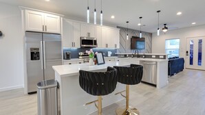 Una cocina moderna con armarios blancos, electrodomésticos de acero inoxidable y una isla central con taburetes de bar.
