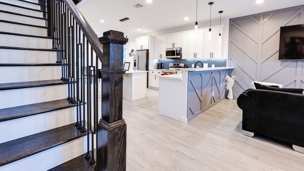 Una cocina moderna con armarios blancos, una isla central y un sofá negro en la zona de estar.