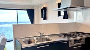 A modern kitchen with a large island, stainless steel appliances, and a view of the ocean. - AZ Hotel Ocean View (Amami)