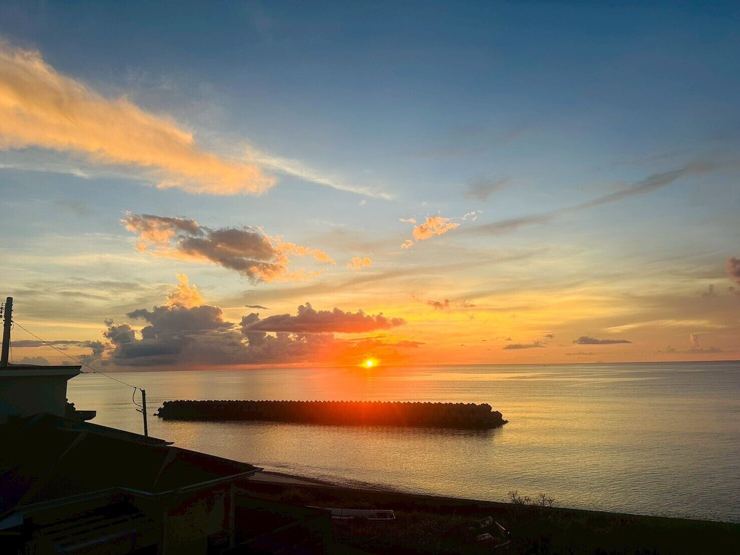 Een zonsondergang boven een rustige zee, met een steiger die het water in reikt.