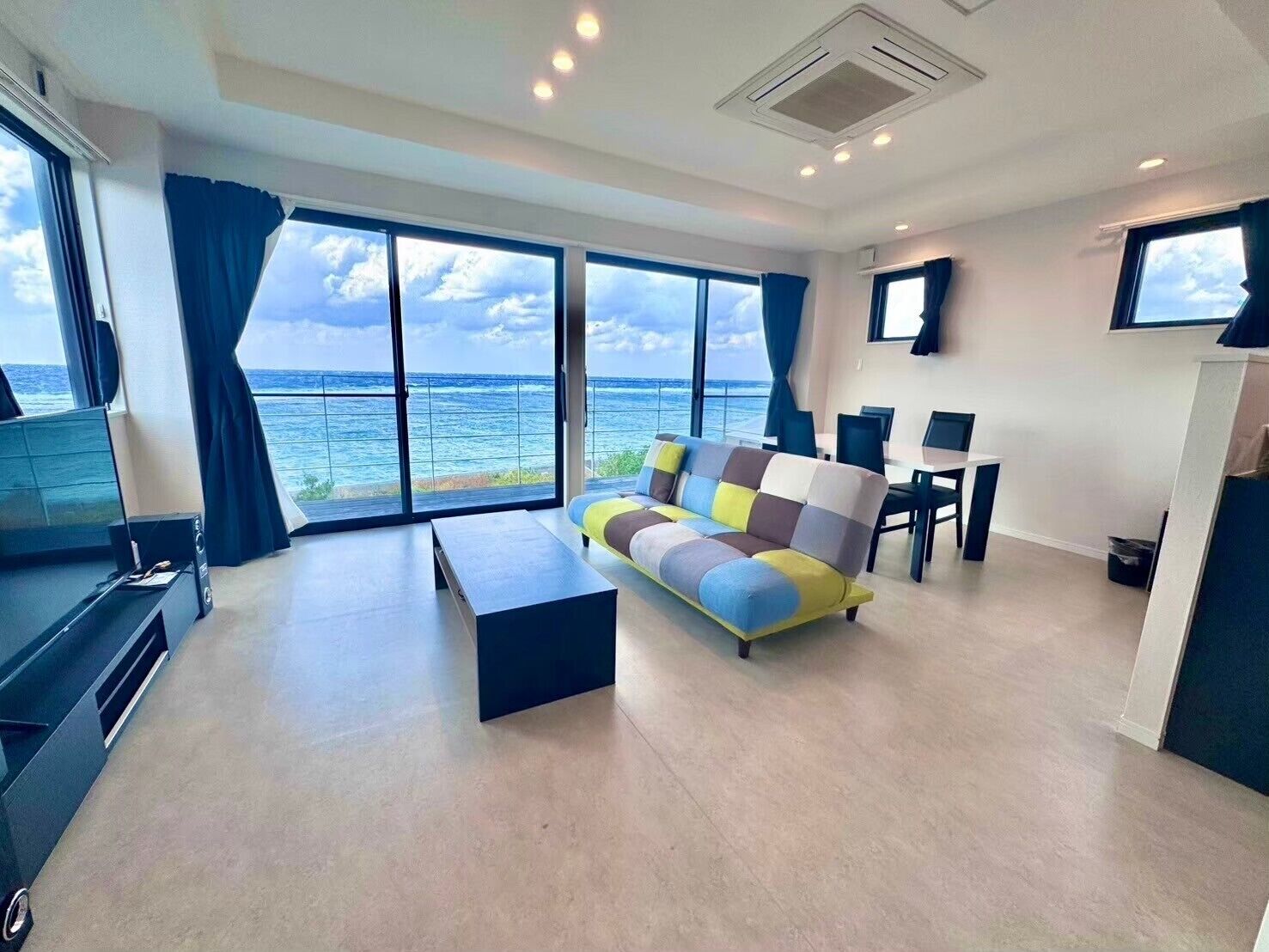 A modern living room with a large window offering a view of the ocean, a sofa, a coffee table, and a dining area with chairs.