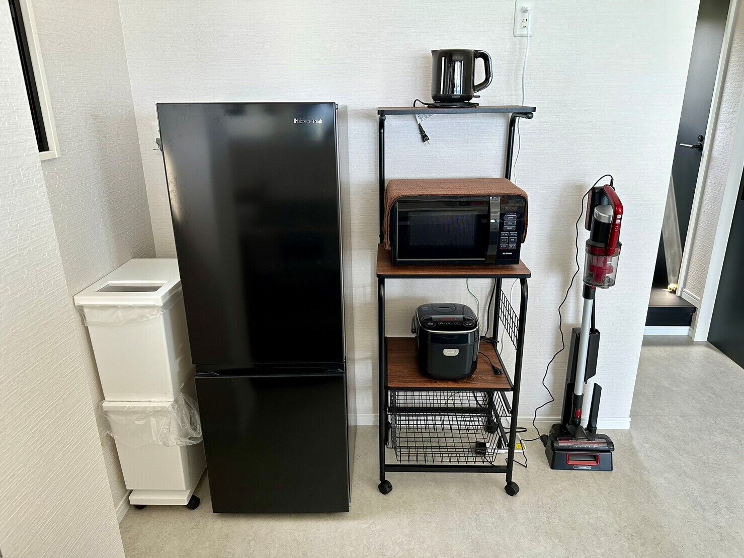 A compact kitchen with a black refrigerator, a microwave, and a coffee maker on a shelf.