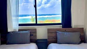 A room with two beds, a window with a view of the ocean, and a curtain. - AZ Hotel Ocean View (Amami)